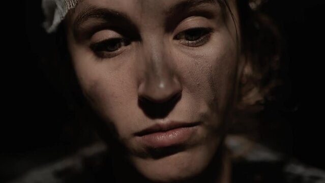 War, accident, fire. Pensive sad wounded woman with dirty face and bandaged head looks tiredly somewhere and touches her head. Close-up