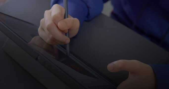 Cut-in shot or b-roll shot of a girl's right hand is drawing and painting on a black tablet with a black digitiser or pen mouse and her left hand is hold a tablet for stability on a black table.