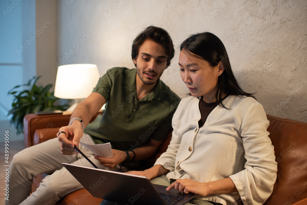 Aufkleber young confident businessman explaining his asian female colleague online data while pointing at lapt