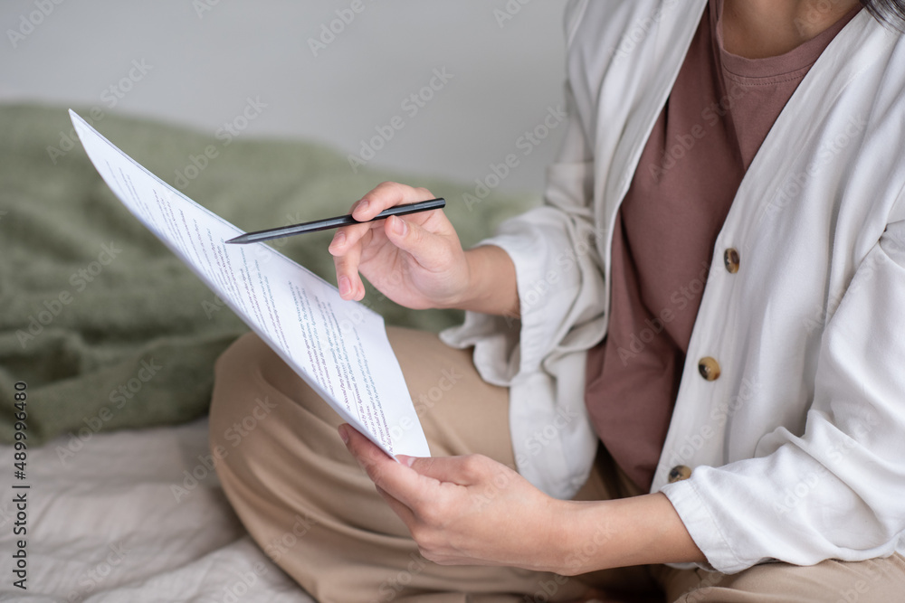 Poster young female auditor in casual apparel pointing at financial paper while looking through text and un