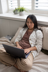 Young serious female analyst in casualwear typing on laptop keyboard and looking through data on screen while working in the net