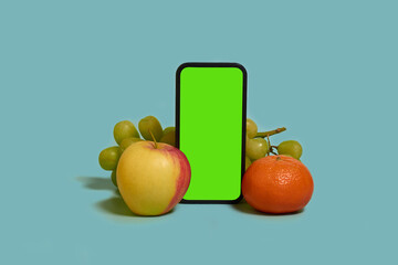 Online shopping. A smartphone with a green screen, mandarine, apple and grapes