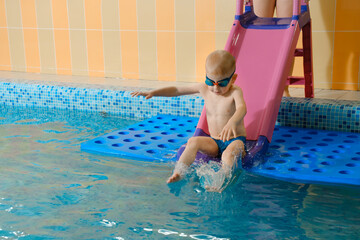 Toddler child learning to dive in indoor swimming pool with teacher. Boy kid sliding into water, balancing and general physical activity for kids in water, early development. Fun and action, splash