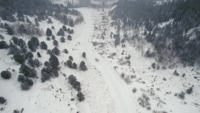 Drone Aerial View of Land Rover Defender D90 SUV Parked on Snow Covered Road in Backcountry Alpine Forest Road in Rocky Mountains near Nederland Boulder Colorado USA During Heavy Snowfall.