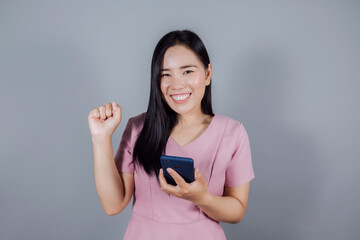 Portrait of happy asian woman holding mobile phone or smartphone on gray background