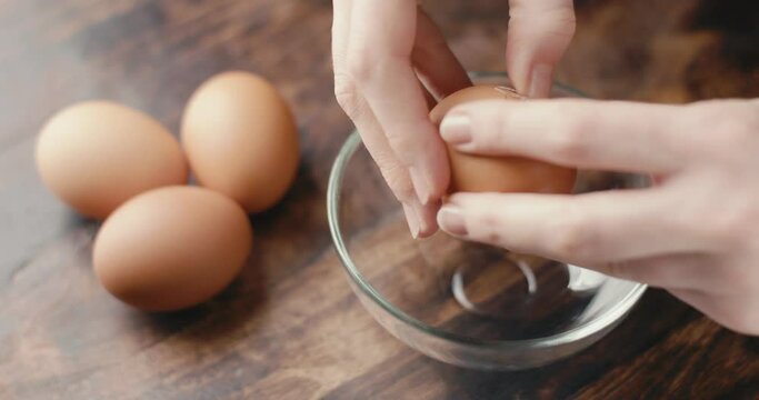 Female hand breaks egg in glass bowl kitchen close up in slow motion