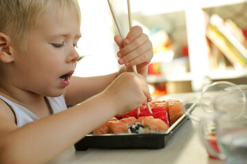 The child is eating sushi. Boy learning to eat rolls with chopsticks.