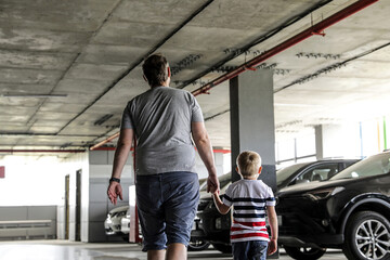 Fototapeta na wymiar Father with a kid are going on the parking to the car. Garage