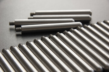 Stainless steel turning parts with thread lie in a row on the table on a black background. Factory, metal processing plant.