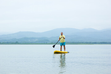 Naklejka premium A young man ride a paddle board on the lake. Supboard water sport activity