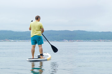 A young man stay on a paddle board on the lake. Supboard water sport activity