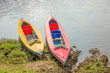 The pair of Kayaks on the river bank. Red and yellow canoe and scenic lake before the trip.