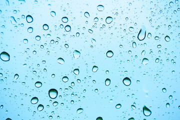 Rain outside the window. Water droplets on a car glass on a background of blue sky and green grass. Overcast. Wet clean nature, ecology