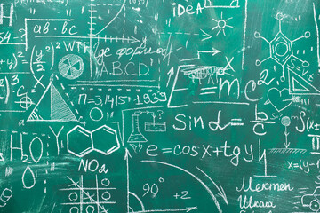 School chalk board is painted with different formulas and signs from the school curriculum. A green...