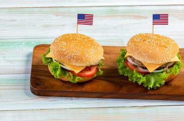 Top view closeup studio shot of two delicious tasty minced pork beef cheeseburgers with small United States of America national flag pinned on bun placed on cutting board on old vintage wooden table