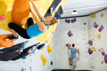 Caucasian woman exercising on wall in climbing gym during bouldering training. © JackF