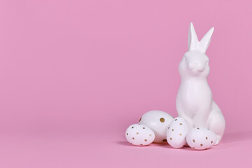White bunny sculpture with easter eggs on pink background with copy space