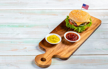 Closeup studio shot two tasty minced beef cheeseburgers on cutting board with small United States of America national flag pinned on bread bun and ketchup mustard cup placed on old retro wooden table
