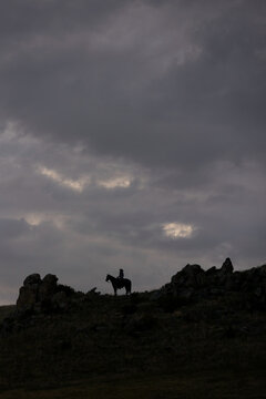 Horseback Cowgirl on rock formation silhouette 