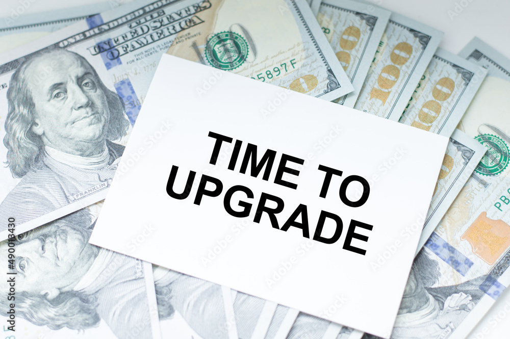Aufkleber the text time to upgrade on a card against the background of paper bills of dollars on the table