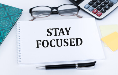 STAY FOCUSED inscription on a notepad on an office desk next to a pen, calculator, glasses, documents