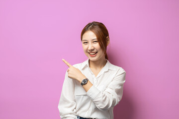 Close up of asian lady smiling, pointing and looking with surprised face, standing on pink...
