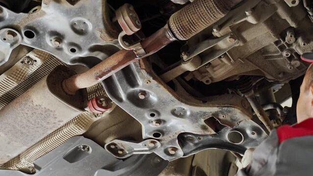 the hands of the master work under the car raised on the lift. view of the gearbox, suspension, subframe, levers, traction, muffler