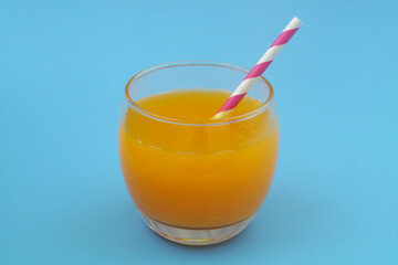 Glass of fresh orange juice with drink straw on blue background