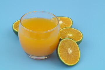 Glass of fresh orange juice and green orange fruits on blue background