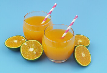 Glasses of fresh orange juice with drink straws and green orange fruits slices on blue background