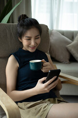Happy young woman typing message on smart phone and drinking coffee.