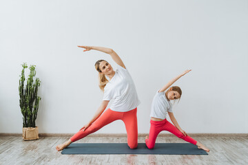 Daughter and mother do yoga together. Women stand in the position of the Gate.Parighasana.Peace and happiness from exercise. Bright room for yoga.