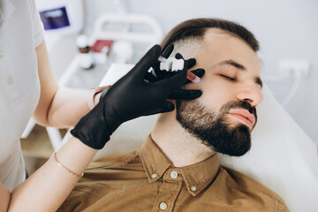Stylish bearded man visiting aesthetic clinic, getting lips filler, closeup. Attractive Man having beauty injection at male spa salon background. Anti-aging treatment for men concept.