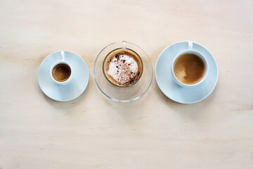 Three cups with various coffee, espresso, cappuccino and lungo crema on a light wooden table, copy space, high angle view from above