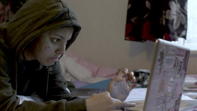 Distance learning concept. Adolescent schoolgirl studying online using laptop. Teen girl school student wearing hoodie watching internet video course sitting at home.