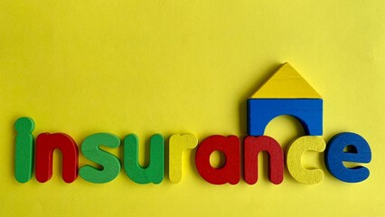 Top view of word Insurance and wooden model house with yellow paper background.