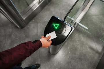Close up of unrecognizable swiping card passing turnstile to enter building. The hand holds the...