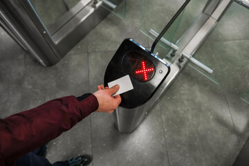 Close up of unrecognizable swiping card passing turnstile to enter building. The hand holds the card. Access denied.