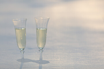 Two glasses of champagne are standing in a snowdrift in the contoured sunlight