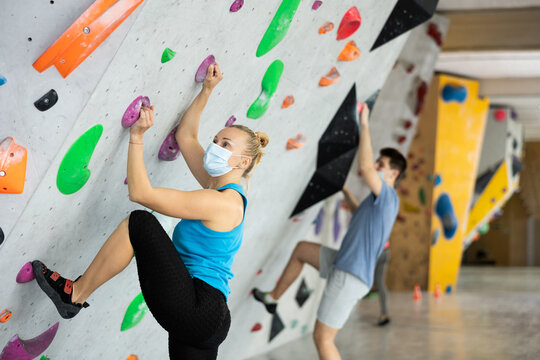 Caucasian woman in face mask exercising on wall in climbing gym during bouldering training. High quality photo