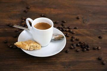 Espresso in a small white coffee cup, spoon and roasted beans on a dark rustic wooden table, copy space, selected focus