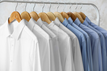 Rack with clean white and blue shirts on light background, closeup