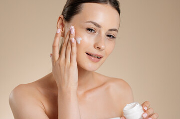 Young adorable woman using moisturising face cream