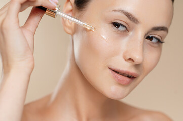 Young woman applying hyaluronic serum on face in studio