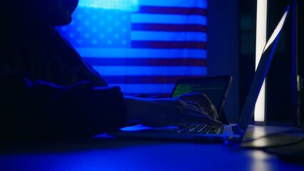 Hacker with laptop and USA flag in background. Cyber attack concept.