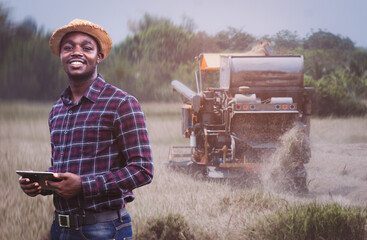 African Farmer holding tablet for combine harvester guidance and control on a background of combine...