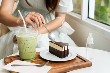 Hands of woman eating chocolate cake and beverage in cafe with alcohol spray on desk. Food and beverage, new normal lifestyle concept. Close up