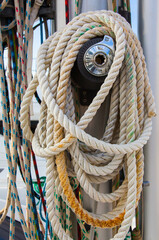 Part of the mast of a sailing yacht, with multi-colored ropes for fastening and a winch mechanism.