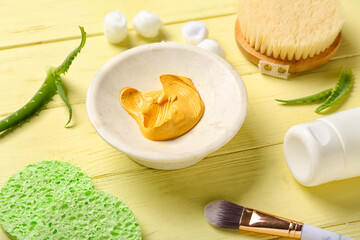 Turmeric mask in bowl, sponges, makeup brush and aloe on color wooden background