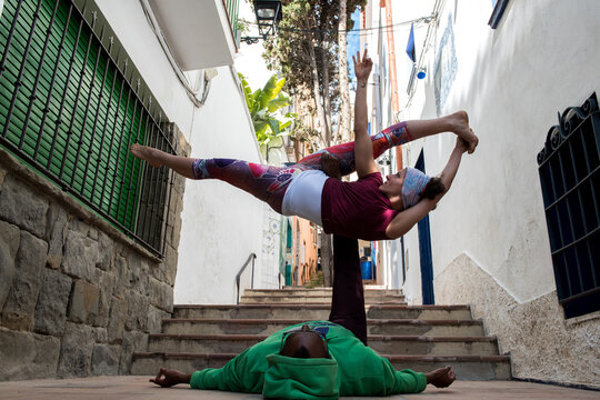 Multiracial couple practice acroyoga on narrow streets with stairs in Sitges